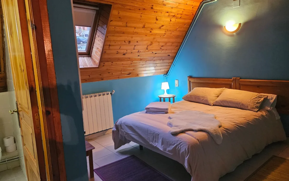 Habitación doble abuhardillada con pared azul y ventana en el tejado