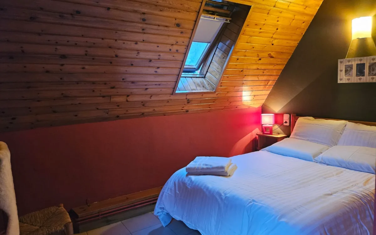 Habitación doble abuhardillada con pared granate y techo de madera
