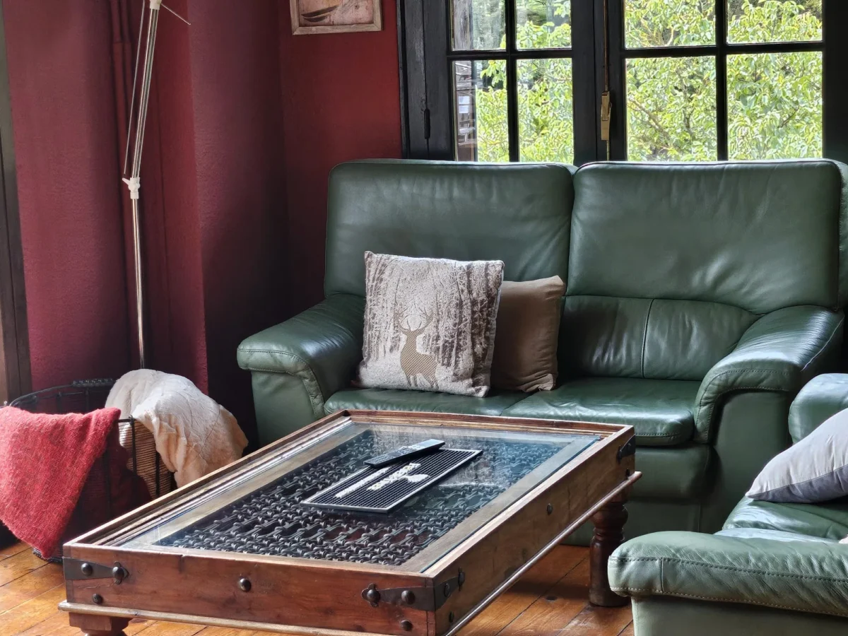 Salón de Hostería Dedieu con sofá de piel verde y mesa de hierro